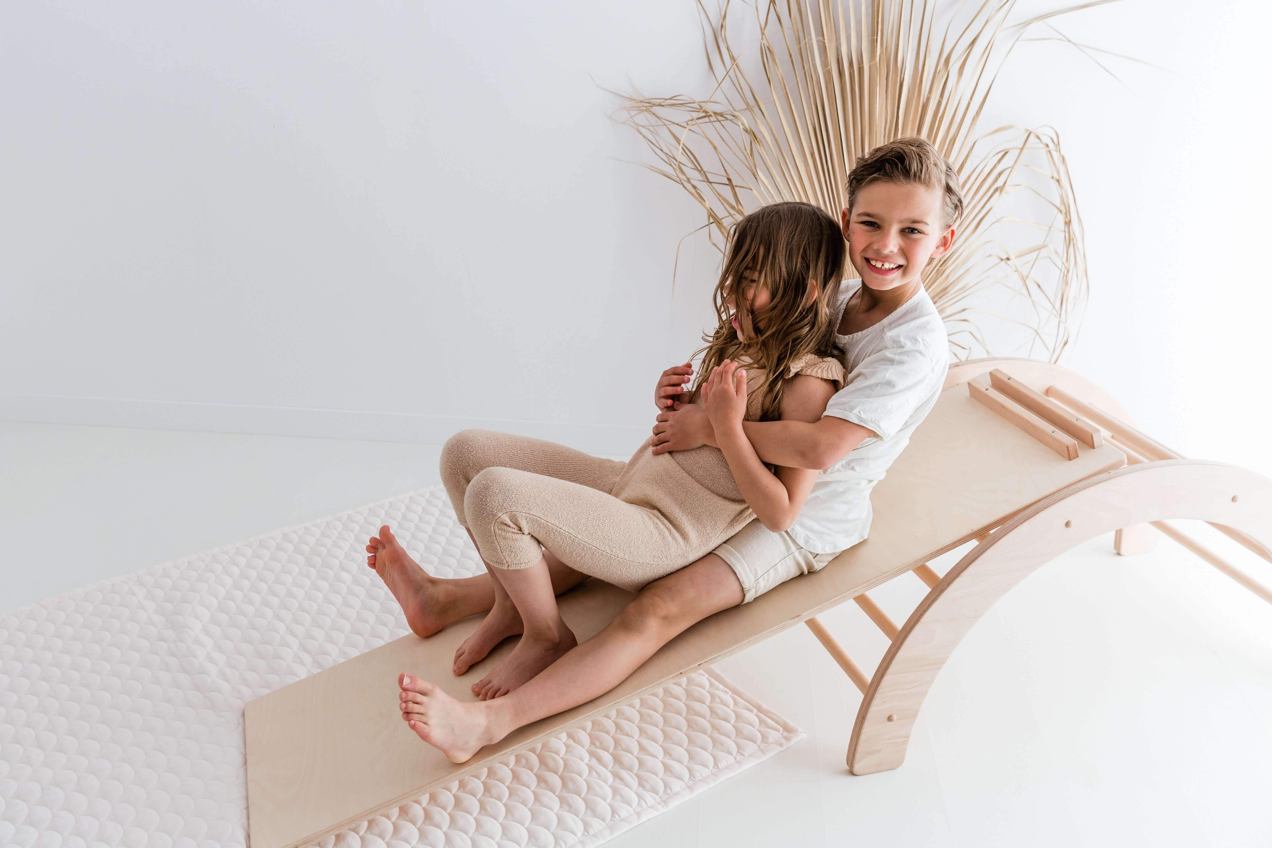 Kinder spielen auf einem stabilen Kletterbogen Pikler Art, der auch als Rutsche genutzt werden kann und pädagogisch wertvolles Holzspielzeug ist.